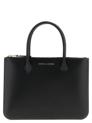 Black cowhide handbag by Comme Des Garçons with sleek design and top handle, shown resting on a surface.