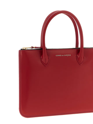 Red cowhide handbag by Comme Des Garçons featuring a structured design and top handle.